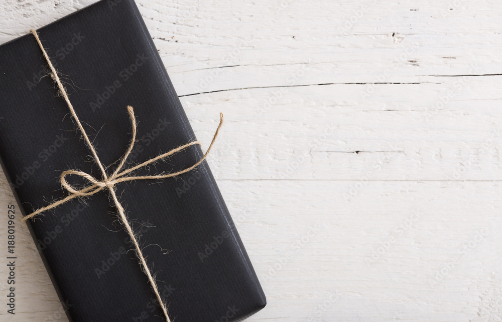 Φωτογραφία Top view on Christmas, birthday or any other celebration gift wrapped in  black paper and decorated with twine on white wooden background