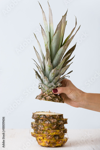 Closeup of woman;s hand holding pineapple. Sliced fruit on light background.