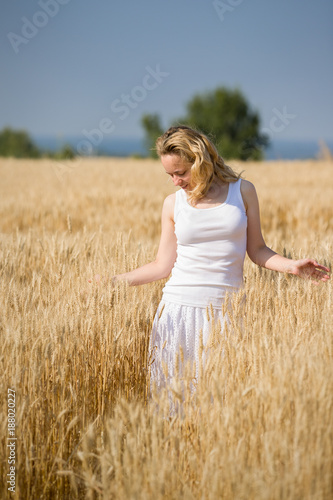 Portrait of young blond smiling woman relaxing while walking on golden wheat field on a summer sunny day. Girl running on rye meadow. Outdoors. Countryside.
