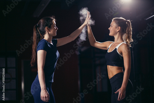 women looking at each other and giving high-five with smile at gym. cross fit and fitness.