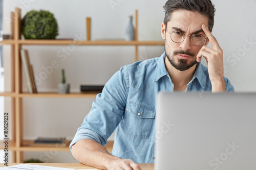 Obraz na plátně Finance director of big cooperation sits at home in his cabinet, reads financial report attentively, sits in front of opened laptop, has serious and concetrated look at screen, works online