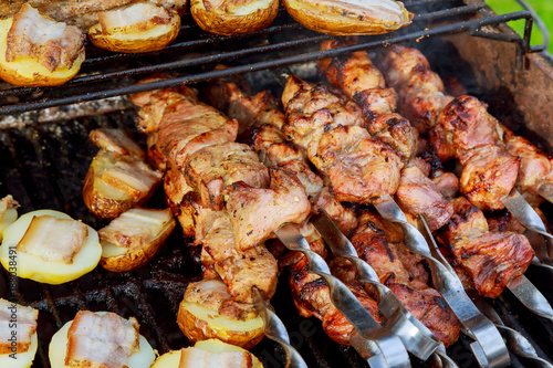 Raw kebab grilling on metal skewer. Meat roasting at barbecue with vegetables. BBQ fresh beef chop slices.