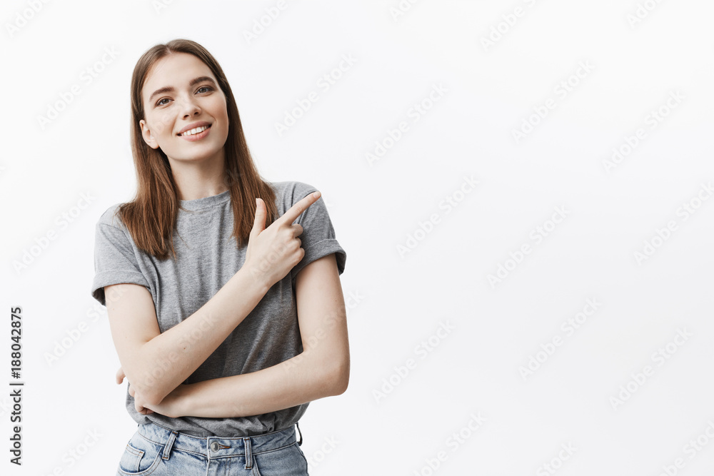 Positive emotions and attitude. Copy space. Good-looking young caucasian brinette student girl with medium hair lenghts smiling brightfully, looking in camera, pointing aside with index finger on Positive emotions and attitude. Copy space. Good-looking young caucasian brinette student girl with medium hair lenghts smiling brightfully, looking in camera, pointing aside with index finger on