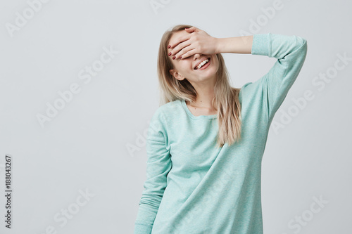 Happy woman with blonde hair closing eyes with hand going to see surprise prepared by boyfriend standing and smiling in anticipation for something wonderful. Young lady covering face with hand