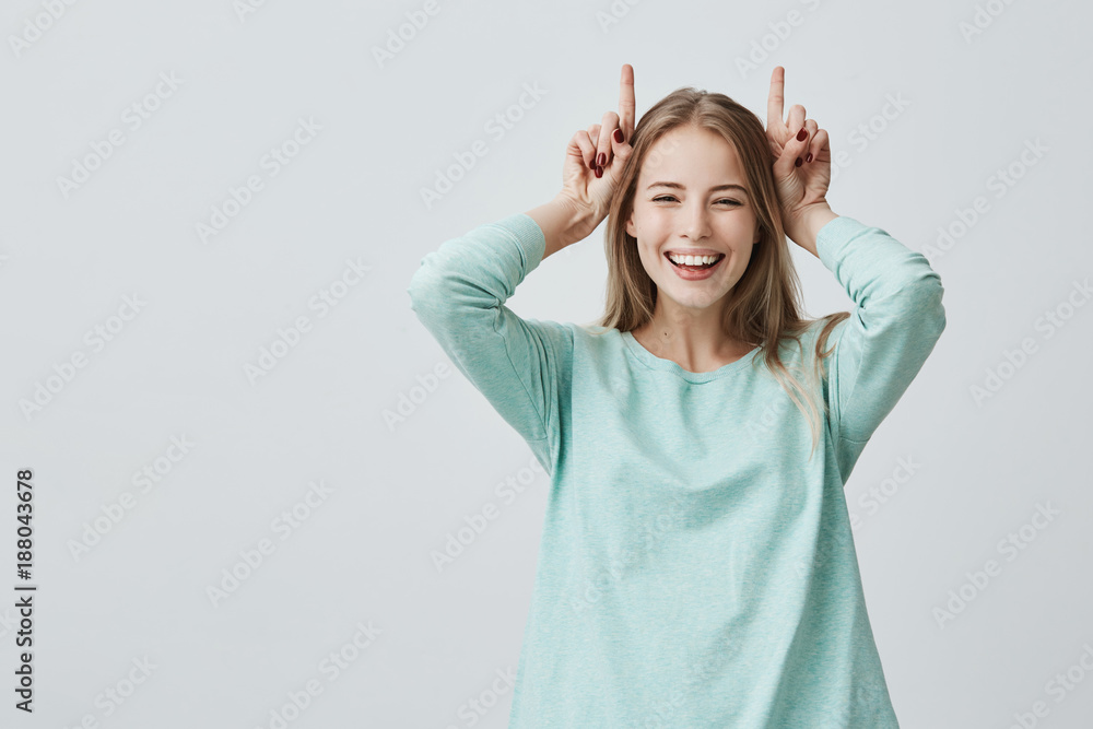 Human face expressions. Body language. Playful funny Caucasian woman with blonde dyed hair smiling broadly holding fingers above head, playing fool and having fun indoors Human face expressions. Body language. Playful funny Caucasian woman with blonde dyed hair smiling broadly holding fingers above head, playing fool and having fun indoors