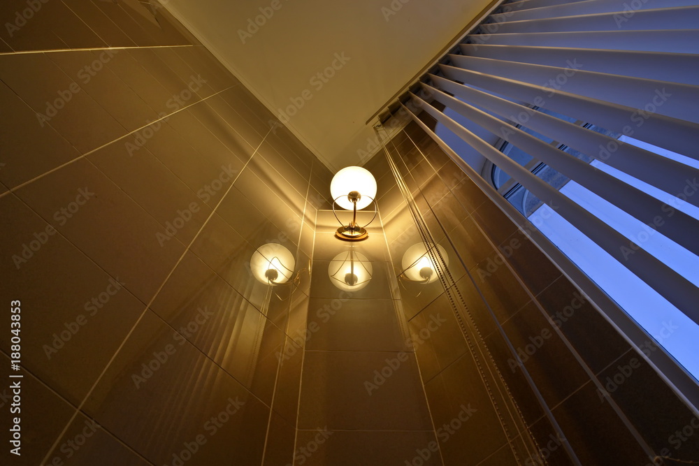 Obraz premium Reflection of the yellow light lamps on the walls in the luxury apartment with the high window and open blind. Bottom view