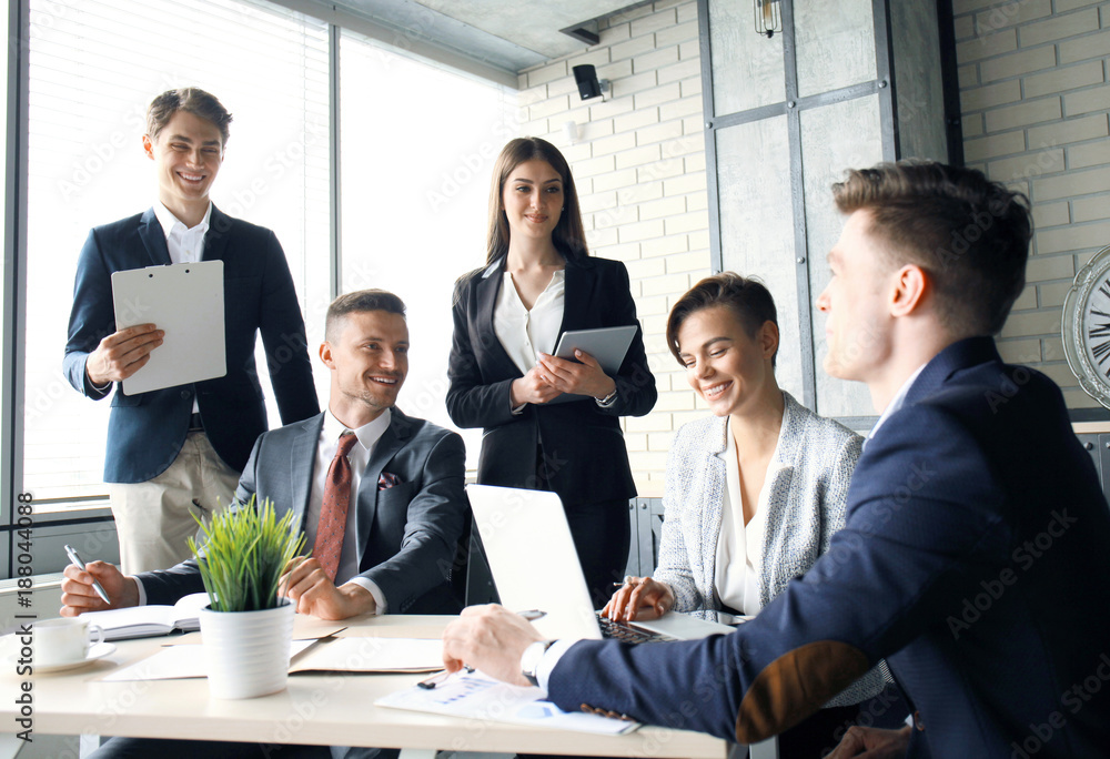Brainstorm. Group of business people looking at the laptop together. One business woman looking at camera. Brainstorm. Group of business people looking at the laptop together. One business woman looking at camera.