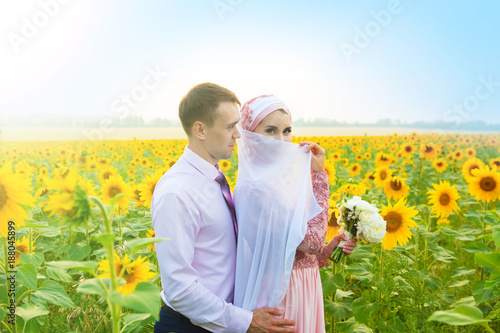 Smiling young islamic couple portrait on sunflowers field. Muslim marriage photo