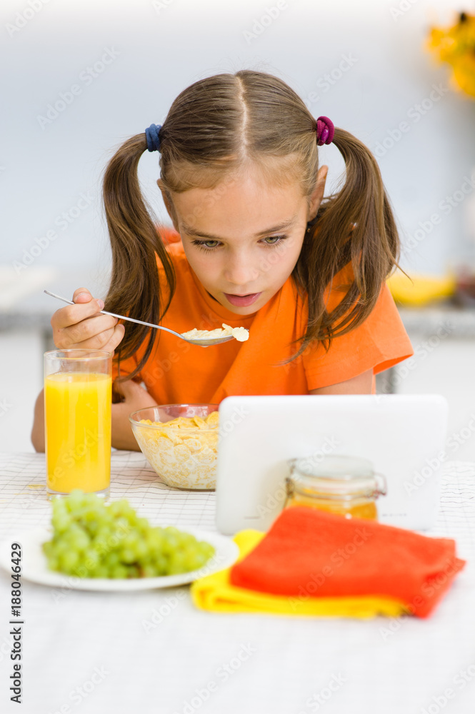 Little girl is having breakfast while watching the movie on the tablet Little girl is having breakfast while watching the movie on the tablet