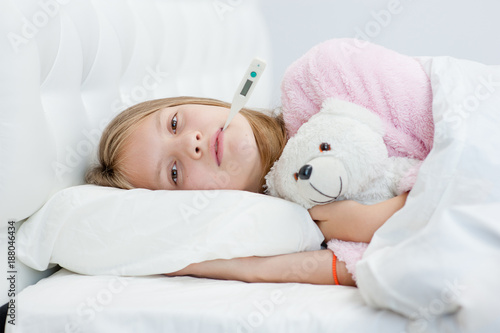 sick girl lying on the bed with a thermometer in mouth