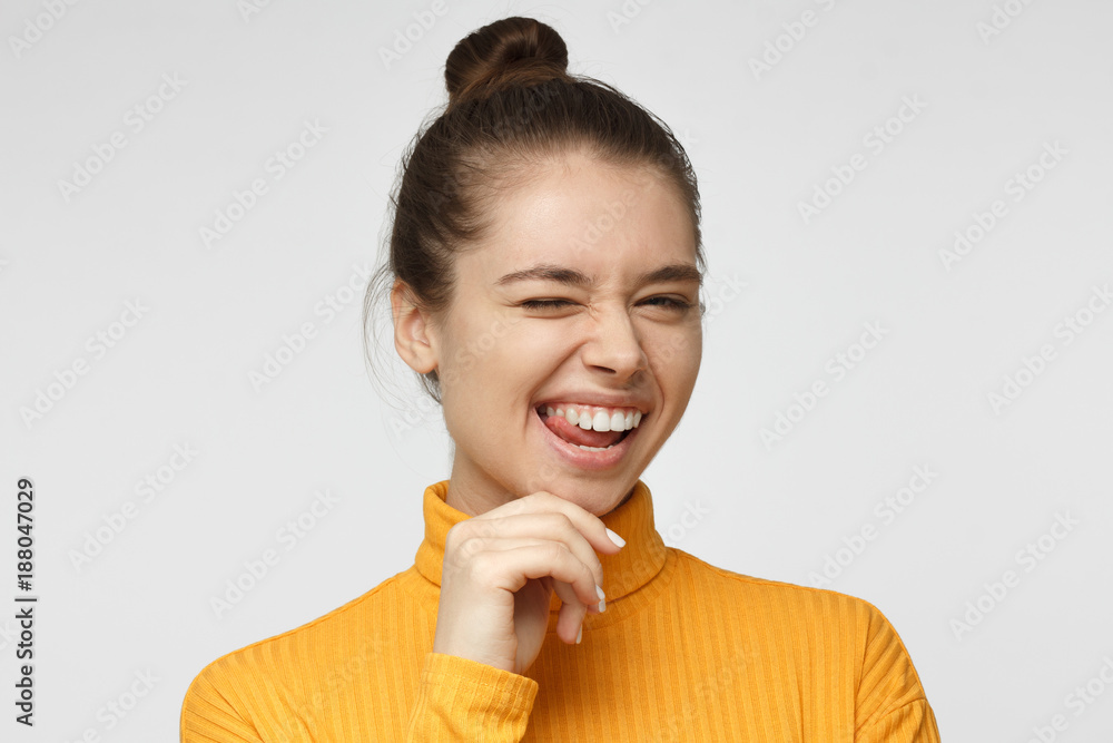 Beautiful girl in bright yellow polo neck sweater smiling and winking, looking at camera isolated on gray background Beautiful girl in bright yellow polo neck sweater smiling and winking, looking at camera isolated on gray background