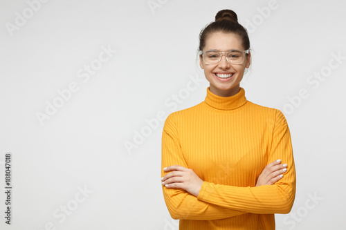 Portrait of attractive young female in yellow sweater standing with crossed arms isolated on gray background. Empty space for your advertsing text