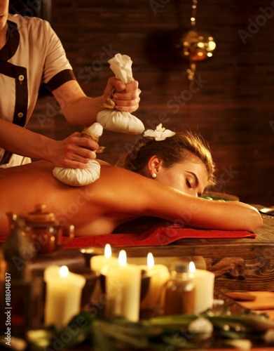 Massage of woman in spa salon. Girl on candles background in spa salon. Luxary interior in oriental therapy salon. Different types of relaxation. Close up of female hands give herbs hot ball therapy.