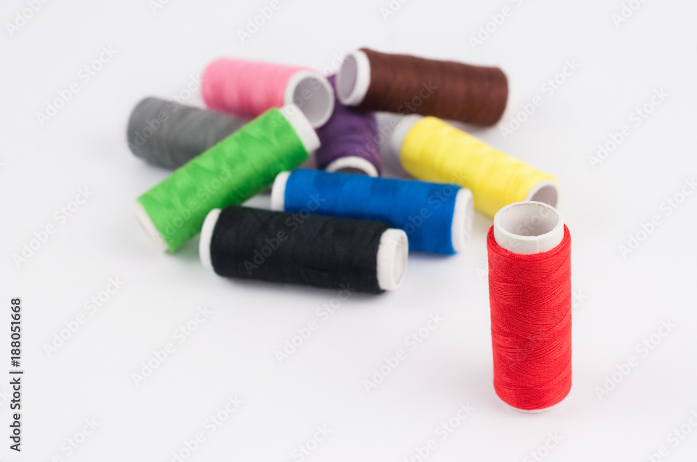 One red bobbin of thread near heap of bobbins of new colorful threads on white background One red bobbin of thread near heap of bobbins of new colorful threads on white background