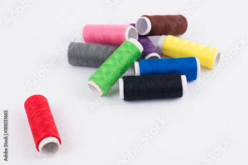 One red bobbin of thread near heap of bobbins of new colorful threads on white background