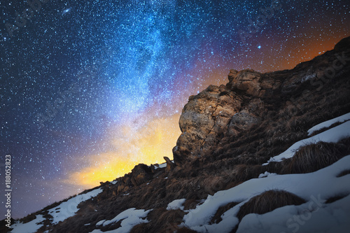 Night scenery done on long exposure. A beautiful Caucasian landscape of red rocks against the background of the cold milky way and a warm yellowish red glow on the horizon behind the rocks.