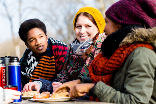 Young friends talking at picnic outdoors in the park in a cold day of winter