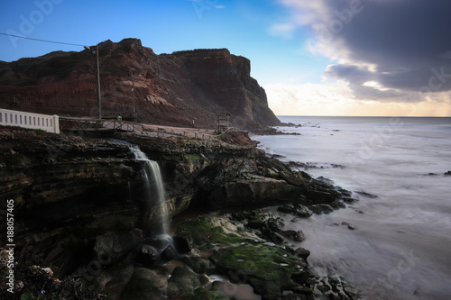 Waterfall runs to the sea in a coastline at the sunset. Long exposure. Portugal