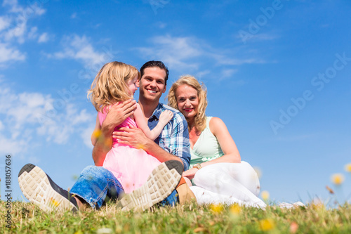 Girl on dads lap, Mom sitting next to them in field