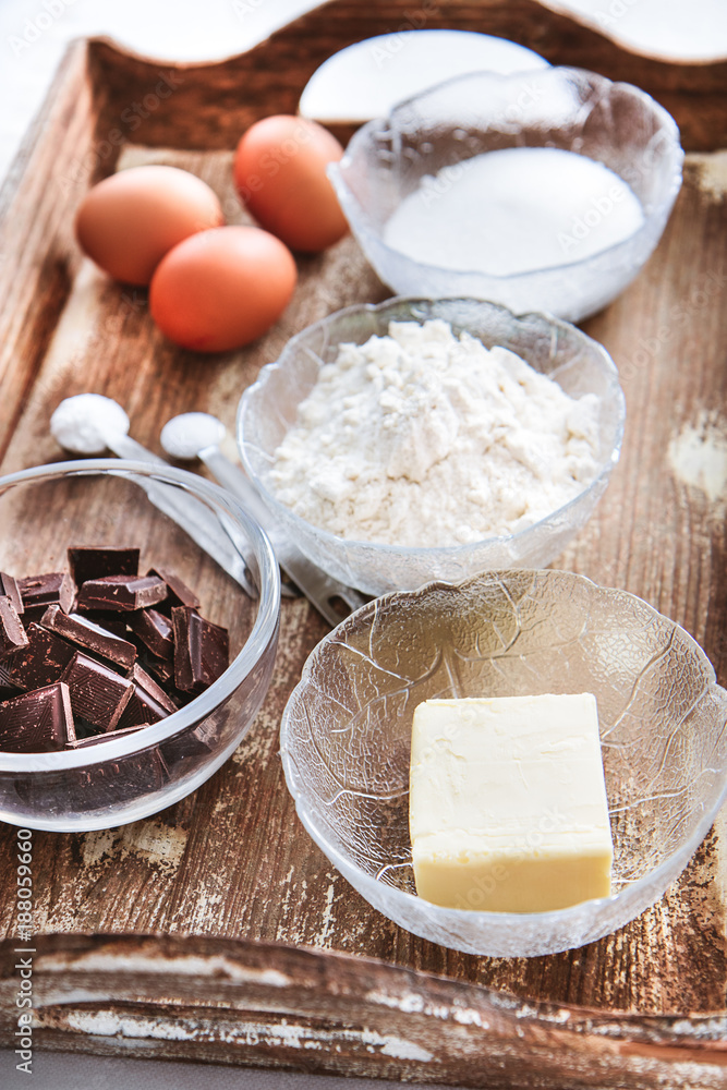 Baking ingredients for chocolate cake muffins or cookies lying ready on wooden kitchen tray. Mise en place, white background, measured ingredients. Baking ingredients for chocolate cake muffins or cookies lying ready on wooden kitchen tray. Mise en place, white background, measured ingredients.