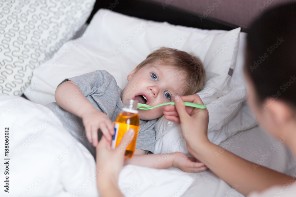 Sick child concept. Mother giving her 2 years old baby boy medicine, cough syrup on a spoon. Sick child concept. Mother giving her 2 years old baby boy medicine, cough syrup on a spoon.