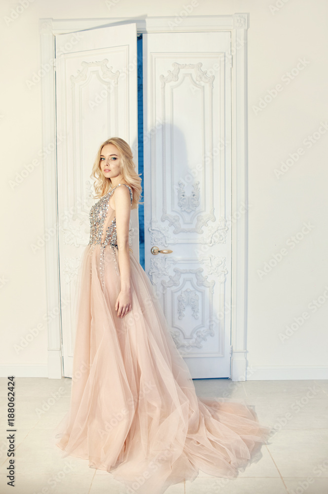 Fashion portrait of a woman in a beautiful long evening dress, near the big white doors. Luxurious interior, perfect figure and hair girl Fashion portrait of a woman in a beautiful long evening dress, near the big white doors. Luxurious interior, perfect figure and hair girl