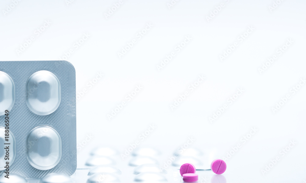 Macro shot of small pink tablets pills and silver aluminium foil blister pack of antihistamine pills on white background and copy space for text. Medicine for asthma treatment concept Macro shot of small pink tablets pills and silver aluminium foil blister pack of antihistamine pills on white background and copy space for text. Medicine for asthma treatment concept