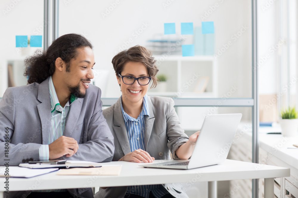 Confident and friendly analyst pointing at laptop display while explaining data to colleague Confident and friendly analyst pointing at laptop display while explaining data to colleague