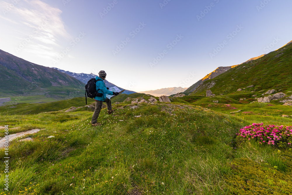 Hiker backpacker with trekking map at sunrise in the italian french Alps.