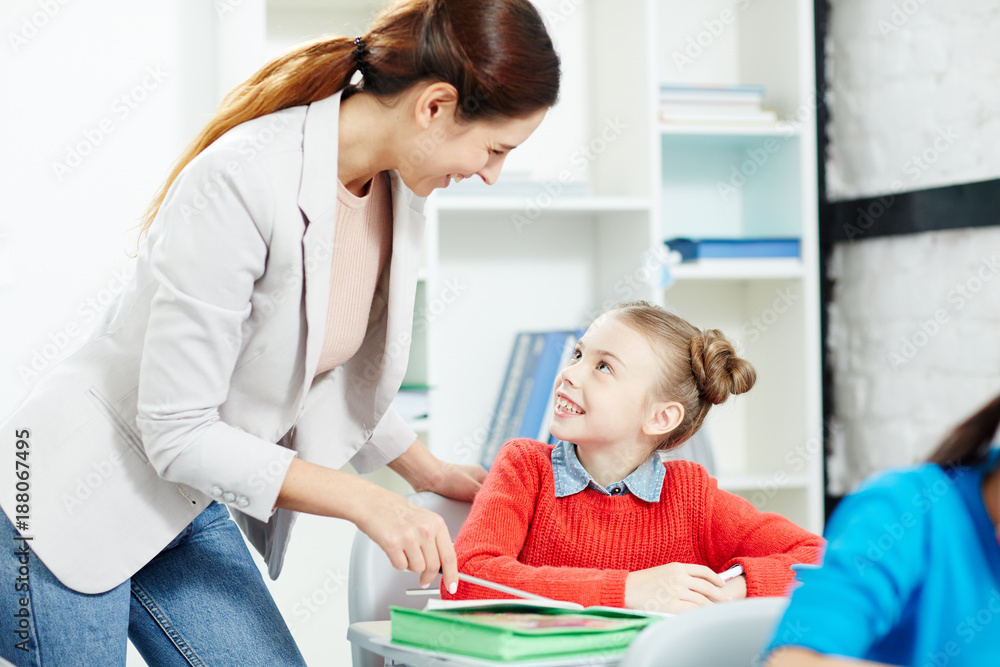 Happy young teacher talking to clever schoolgirl during individual work at lesson Happy young teacher talking to clever schoolgirl during individual work at lesson