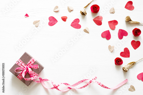 Gift box with a pink tape and a bow in an environment of decorative hearts on a wooden white background. Romantic card. Gift by St. Valentine's Day. © isavira