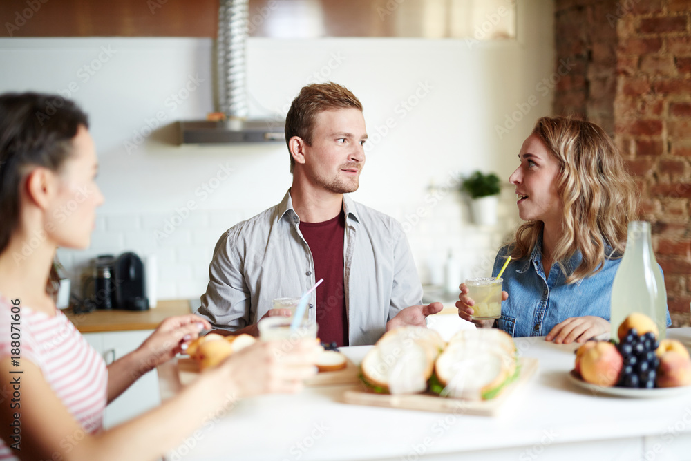 Small group of friends with drinks having talk in the kitchen while having homemade snack Small group of friends with drinks having talk in the kitchen while having homemade snack