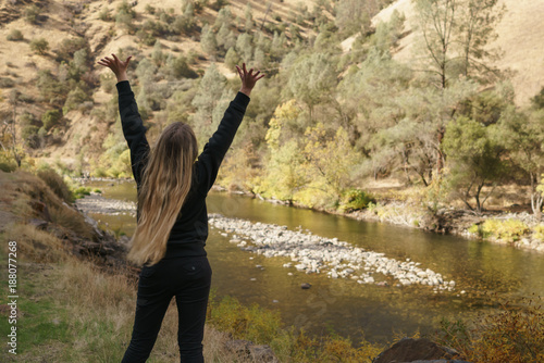 teen girl standing with raised hands near merced river on warm autumn day