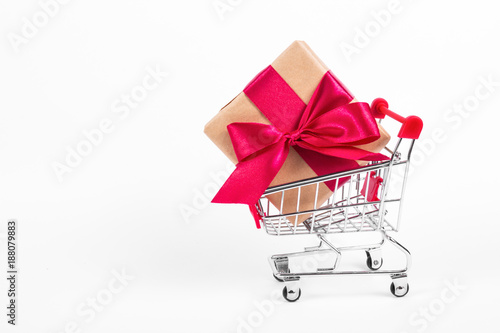 Gift box with bow in shopping trolley. Shopping cart with large gift box on white background