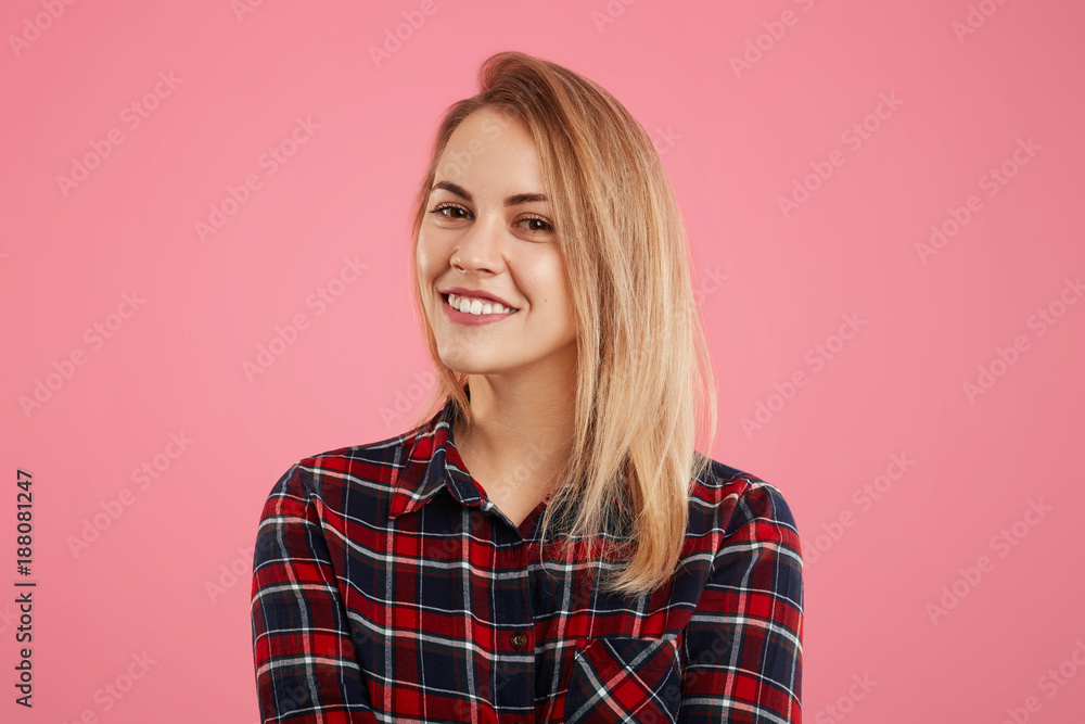 Pretty adorable woman with pleasant smile looks directly into camera, dressed in checkered shirt, isolated over pink background. Smiling friendly young female rejoices her success, poses indoor Pretty adorable woman with pleasant smile looks directly into camera, dressed in checkered shirt, isolated over pink background. Smiling friendly young female rejoices her success, poses indoor