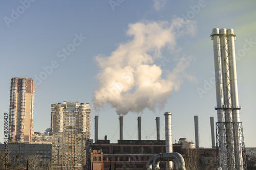 Large smoking chimneys of a plant, against a blue sky background