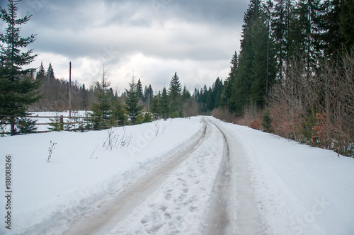 Winter road with traces in the forest. Thoroughfare covered with snow in the winter forest in the mountains.