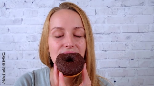 Joyful young woman eating a chocolate donut and drinking tea photo