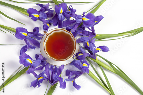 Fototapeta Naklejka Na Ścianę i Meble -   Violet Irises xiphium (Bulbous iris, sibirica) with cup of tea on white background with space for text. Top view, flat . Holiday greeting card for Valentine's Day, Woman's Day, Mother's Day, Easter!
