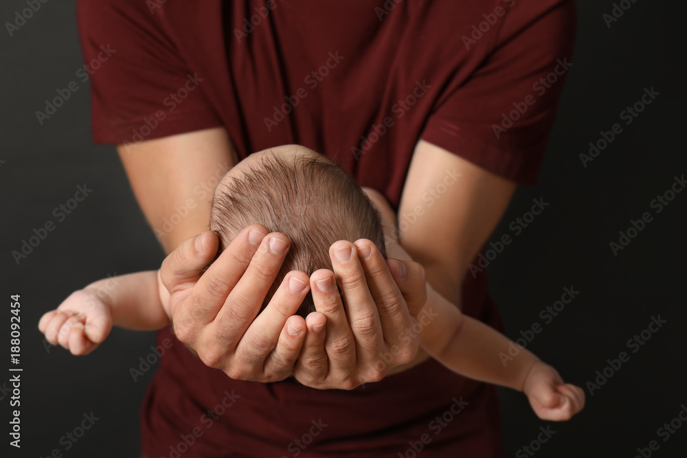 Father with cute little baby on dark background