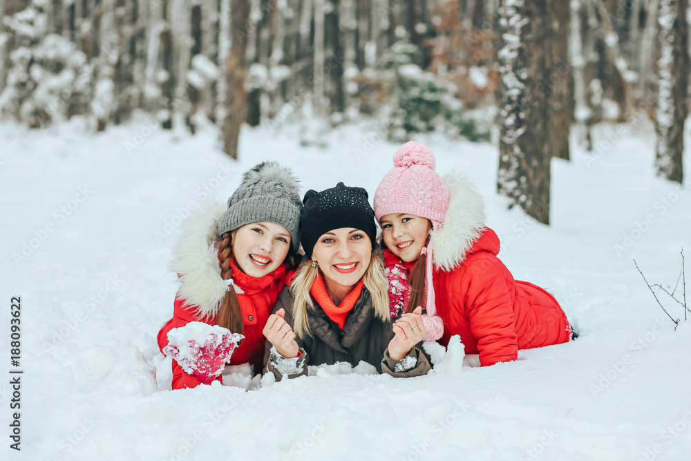 happy family on winter vacation in the forest. A young mother with two daughters in the forest lie on the snow