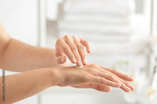 Young woman applying cream on hand against blurred background