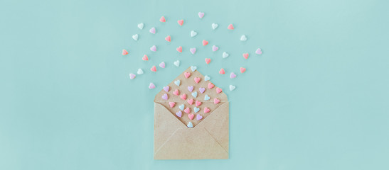 Multicolor sweets sugar candy hearts fly out of craft paper envelope on the light blue background . Valentine day. love concept. Gift, message for lover. Space for text. Wide banner.