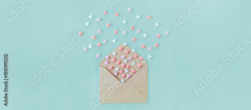 Multicolor sweets sugar candy hearts fly out of craft paper envelope on the light blue background . Valentine day. love concept. Gift, message for lover. Space for text. Wide banner.
