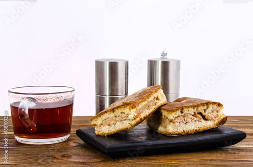 pie with fish and a cup of tea salt shaker and pepper on a black tray on a wooden table