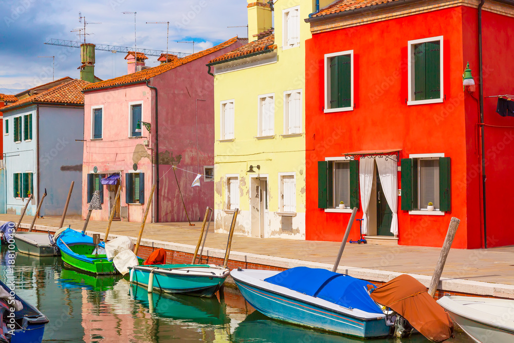 Colorful houses and boats in Burano island with cloudy blue sky near Venice, Italy. Popular and famous tourist place