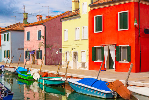 Colorful houses and boats in Burano island with cloudy blue sky near Venice, Italy. Popular and famous tourist place