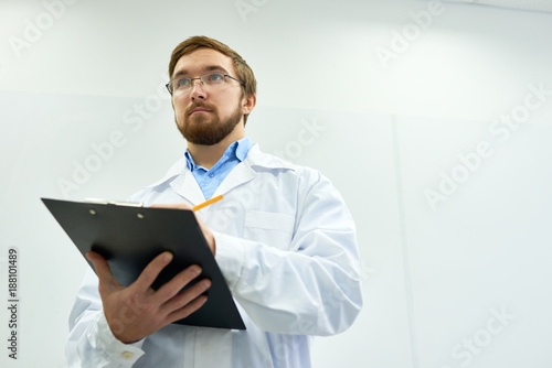Tableau sur toile Low angle  portrait of young bearded doctor wearing glasses standing against whi