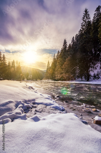 frozen river among conifer forest with snow on the ground in carpathian mountains in evening light © Pellinni