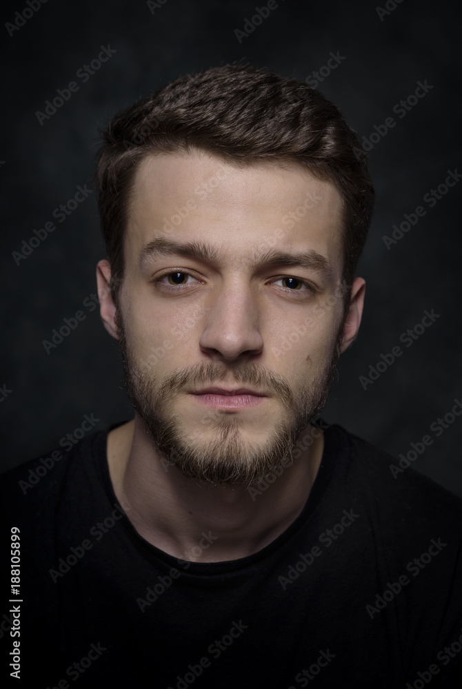 Portrait of a young man with a beard on a dark background.